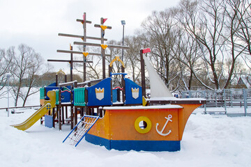 Children's playground with swings and rides in a winter snow-covered park.