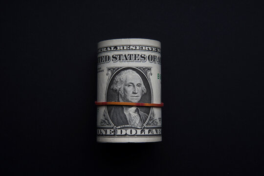 Money rolls wrapped with red rubber band isolated on black background. One Dollar is a portrait of the late George Washington, the first president of the United States. Bank image and commercial photo