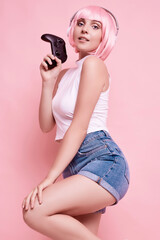 Happy sexy gamer girl with pink hair playing video games using joystick
