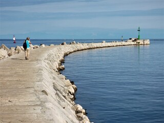 Muelle de un puerto pesquero en el Mar Adriático, con personas paseando o pescando y una baliza verde al fondo