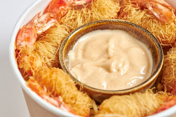 Close-up of a cube of fried prawns wrapped in Kataifi pasta and served with dragon sauce.