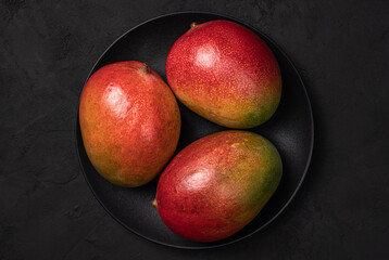 Fototapeta na wymiar Three mango fruits on the black plate.Top view.Dark food phhotography.