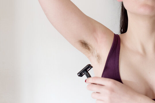 Una mujer joven se afeita las axilas peludas sin depilar con una maquinilla de afeitar negra eco friendly de acero inoxidable. Concepto de depilaci&oacute;n femenina. Enfoque de primer plano selectivo.