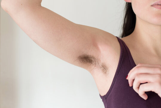 Mujer joven levantando su brazo y mostrando la axila con pelo negro sin afeitar. Concepto bodypositive, feminismo y cuidado corporal. Hermosas axilas femeninas peludas