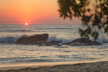 Wave crashing on a rock during the sunset seen from the beach