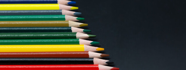 Colorful pencils made of wood slanted together with dark background and copy space for free text in panorama format