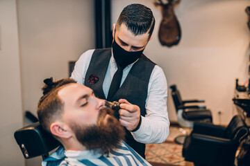 Young good looking hipster man visiting barber shop. Trendy and stylish beard styling and cut.