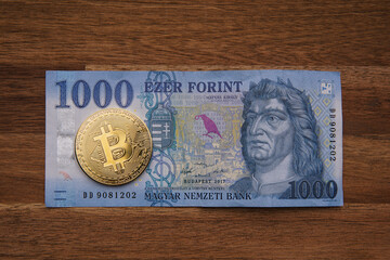 1000 Hungarian forints cash Portrait of King Mátyás. Brown wooden table. Next to it is a gold bitcoin digital cryptocurrency coin. Bank image and photo