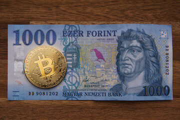 1000 Hungarian forints cash Portrait of King Mátyás. Brown wooden table. Next to it is a gold bitcoin digital cryptocurrency coin. Bank image and photo