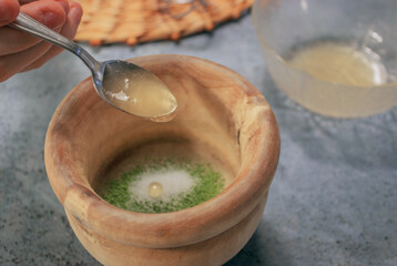 Horizontal image of clay bowl full of matcha tea in powder with sugar while putting honey with a...