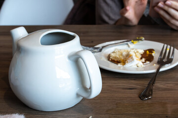 A white ceramic mug beside a plate of cake crumbs with two silver forks on a hardwood table, February 2021, in a small local cafe.