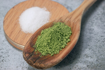 Horizontal image of a detail of many matcha tea in powder on top of a wooden cooking stick with a little sugar. Matcha tea preparation 2021.