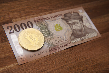 Hungarian forint 2000 forint banknote Gábor Bethlen portrait. Brown wooden table. Next to it is a gold bitcoin digital cryptocurrency coin. Bank image and photo.