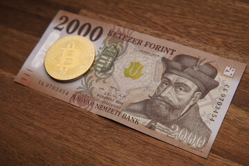 Hungarian forint 2000 forint banknote Gábor Bethlen portrait. Brown wooden table. Next to it is a gold bitcoin digital cryptocurrency coin. Bank image and photo.