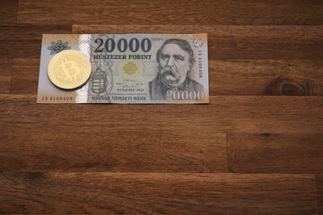 Hungarian forint 20 000 forint banknote Ferenc Deák. Brown wooden table. Next to it is a gold bitcoin digital cryptocurrency coin. Bank image and photo.