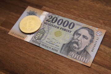 Hungarian forint 20 000 forint banknote Ferenc Deák. Brown wooden table. Next to it is a gold bitcoin digital cryptocurrency coin. Bank image and photo.