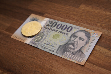 Hungarian forint 20 000 forint banknote Ferenc Deák. Brown wooden table. Next to it is a gold bitcoin digital cryptocurrency coin. Bank image and photo.