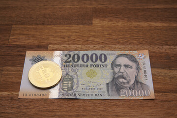 Hungarian forint 20 000 forint banknote Ferenc Deák. Brown wooden table. Next to it is a gold bitcoin digital cryptocurrency coin. Bank image and photo.
