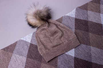 Fototapeta na wymiar set of hat and stole knitted by hand. A hat with a fur pompom. Brown, beige, white colors.