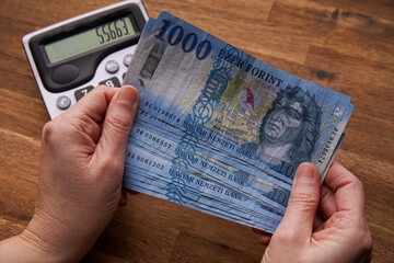 Woman hand holding cash Hungarian forint banknotes, business calculations and expenses, business and people concept. Female hand holding money. The calculator on the wooden table.