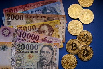 Several Hungarian forint paper money denominations with a gold bitcoin digital cryptocurrency coin on a blue background. Bank image and photo.