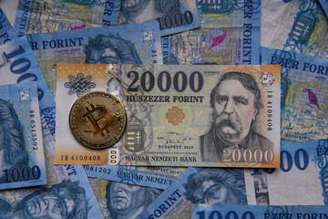 Hungarian banknotes and bitcoin (BTC) digital cryptocurrency coins on a blue background from 1000 HUF paper money.