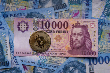 Hungarian banknotes and bitcoin (BTC) digital cryptocurrency coins on a blue background from 1000 HUF paper money.