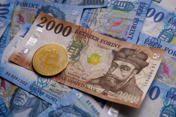 Hungarian banknotes and bitcoin (BTC) digital cryptocurrency coins on a blue background from 1000 HUF paper money.