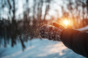 close up of female hands in mittens clapping with snow in winter sunny park