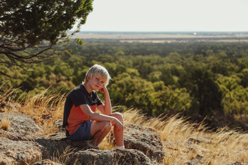Naklejka na ściany i meble Young boy relaxing on rock with sweeping scenic view in background