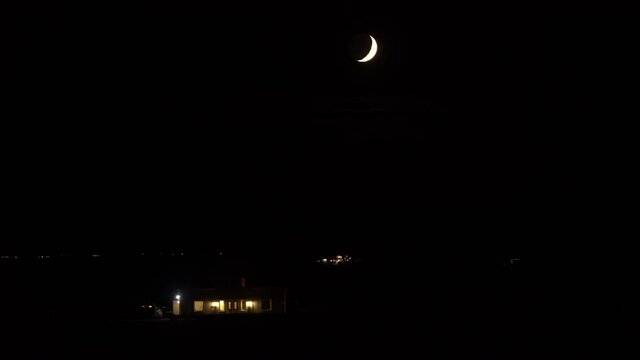 Car driving past country house under crescent moon dark night Iceland