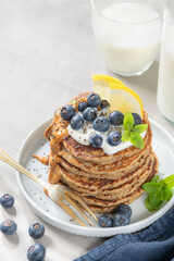 Healthy summer breakfast, homemade classic american pancakes with fresh blue berries, lemon, yogurt and peanut butter. Morning light grey stone background.