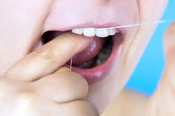 Woman brushing teeth with dental floss, close-up.