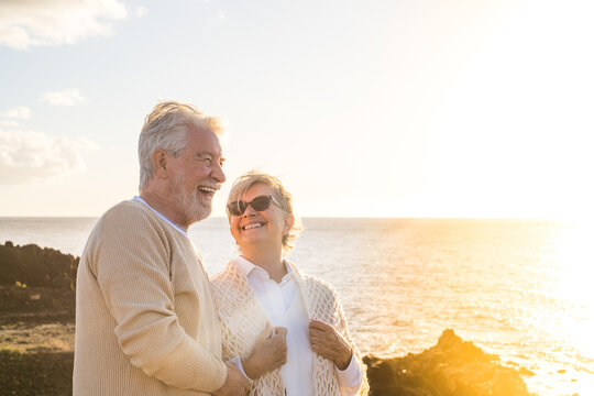 close up and portrait of two happy and active seniors or pensioners having fun and enjoying looking at the sunset smiling with the sea - old people outdoors enjoying vacations together.