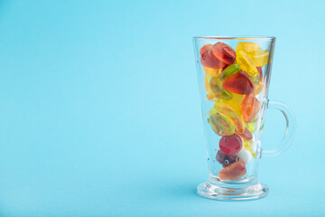 Various fruit jelly candies in drinking glass on blue background. copy space, side view.