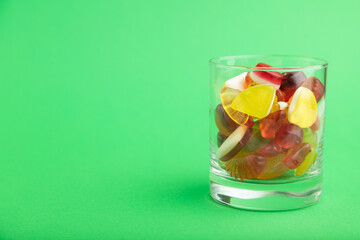 Various fruit jelly candies in drinking glass on green background. copy space, side view.
