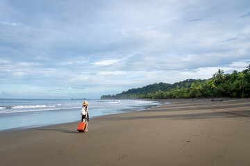 Woman with orange luggage walking along ocean beach