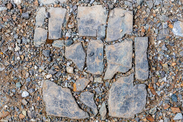 A dirty broken stone tile on gravel. The tile is arranged to it is obvious how it fit together before it was broken. Some bits missing.