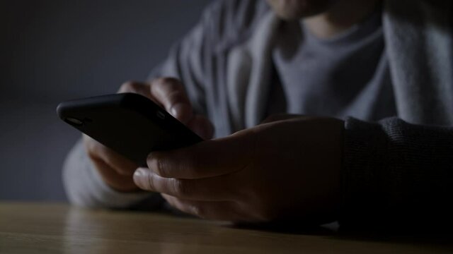 暗い部屋でスマートフォンを操作している男性