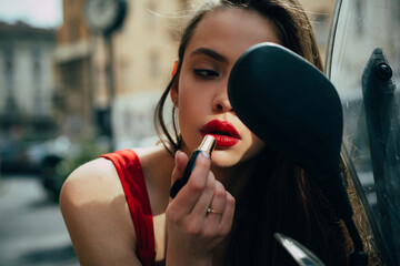 Fashion girl with red lips put lipstick looking in a rear. Street fashion. City life. Makeup in...