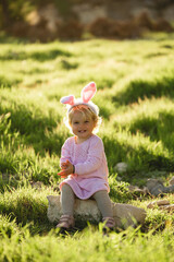 Happy and cute baby girl wear rabbit ears. The girl has blonde curly hair and a pink dress. Easter concept. 