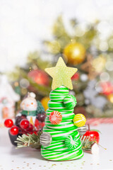 Caramel candy Christmas tree. Christmas card concept. Striped christmas caramel tree with golden star on top. Light up natural green fir tree with bokeh in background. Candle, holly berries, confetti.