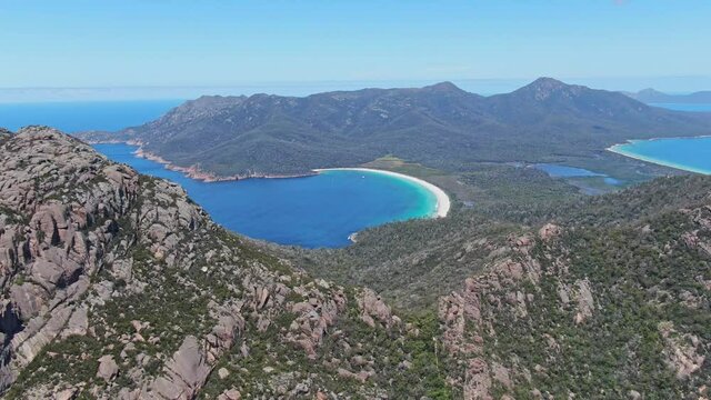 High angle panoramic aerial drone footage of the Freycinet Peninsula and National Park with famous Wineglass Bay in Tasmania, Australia. The Hazards mountain range with Mount Amos in the foreground.
