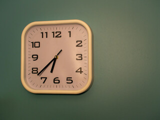 square shape white wall watch hanged on the green wall