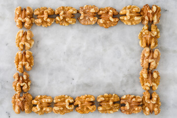 Fresh raw walnut halves shaped in a frame on a marble background
