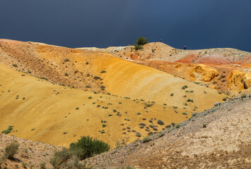 A multicolored desert relief in the mountains in the south of Altai. Against the background of a dark stormy sky.