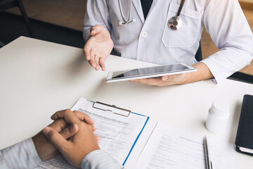 Asian doctor talking the patient at clinic while using the tablet explaining the patient condition and the treatment result.