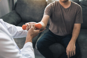 Asian young male physiotherapist helping patient with lifting dumbbells exercises in office.
