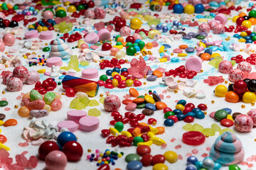 Multi-colored candy balls on icing sugar table. Candy sweets background made of assorted chocolate coated and jelly beans. Various shaped delicious sugary treats. Holiday festive background.