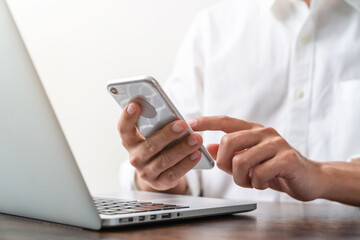 Woman hand using smartphone and laptop on the table in office.